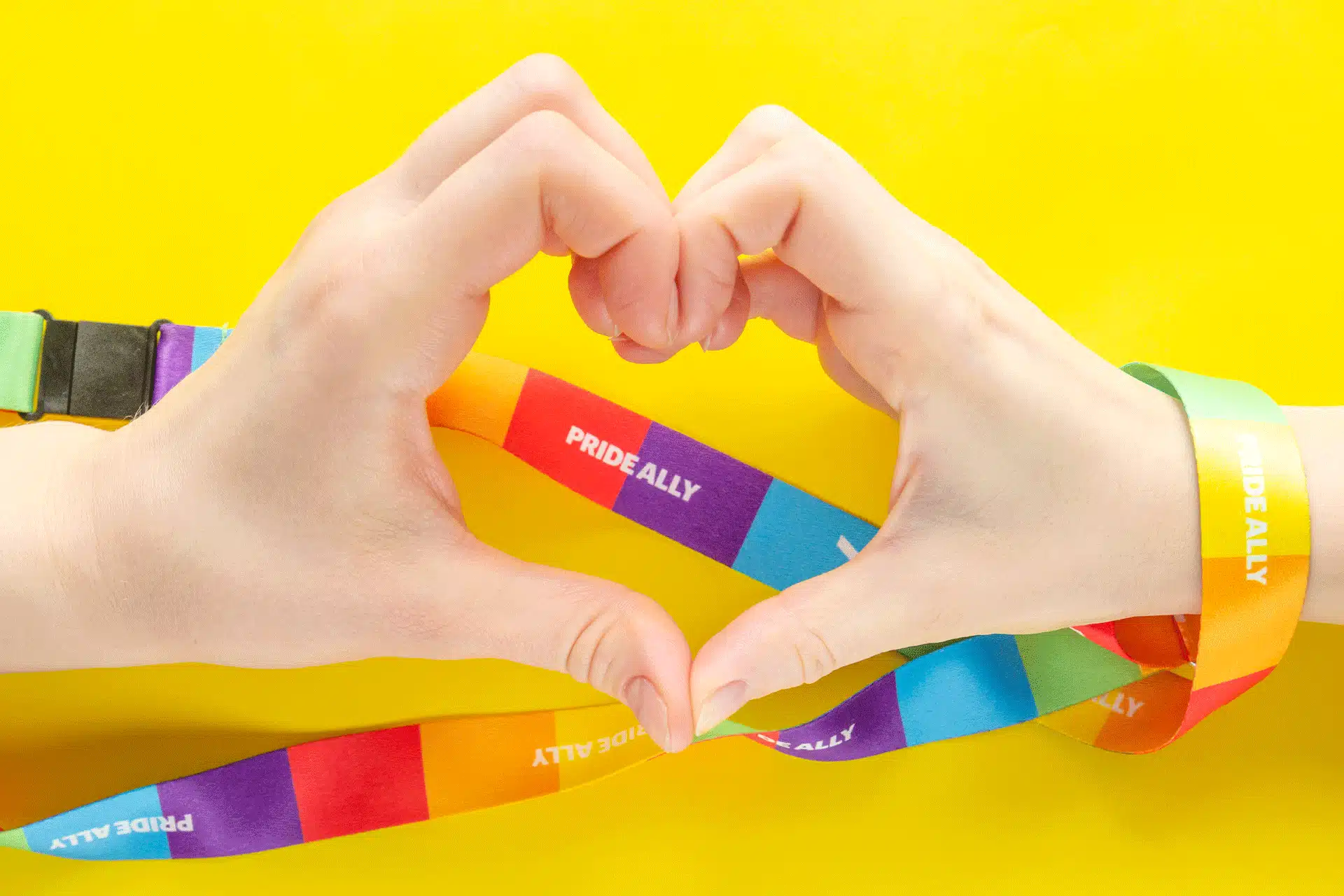 Two hands making a heart with a rainbow pride lanyard to demonstrate allyship in the workplace.